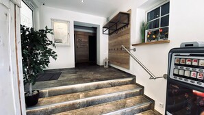Una escalera con acabado de madera, una planta en maceta, una puerta con un letrero y un estante de pared con adornos.