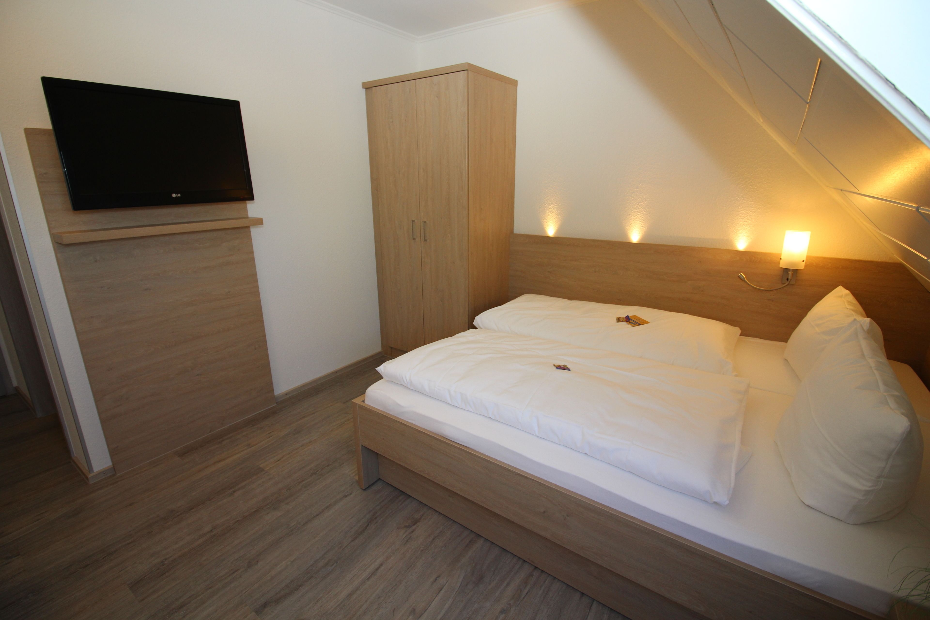 Ein Schlafzimmer mit Bett, Kleiderschrank, Wandfernseher und Nachttischlampe.