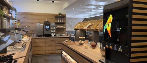 A modern café with a wooden counter, coffee machines, and a variety of food items displayed.