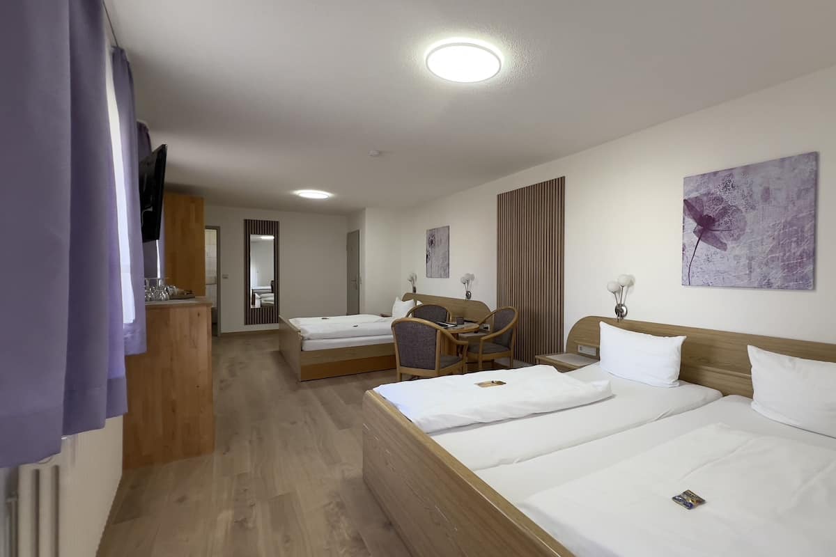 Habitación de hotel con dos camas, un escritorio, sillas, un espejo y obras de arte en las paredes.