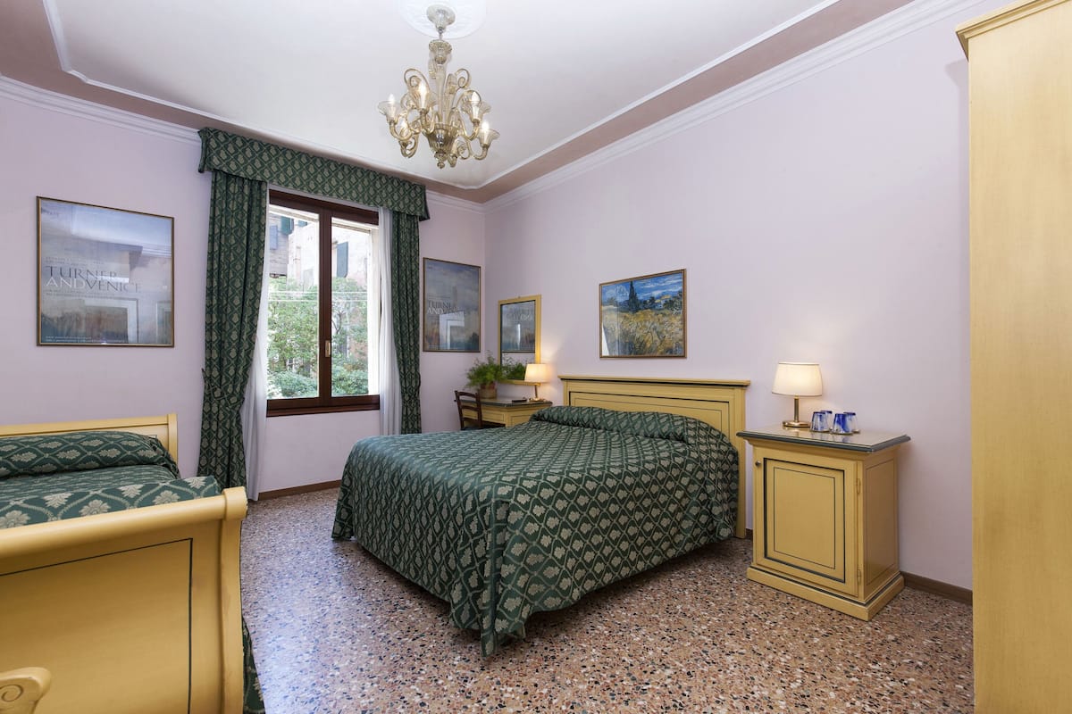 A bedroom with a bed, a nightstand, a dresser, a chandelier, and framed pictures on the wall.