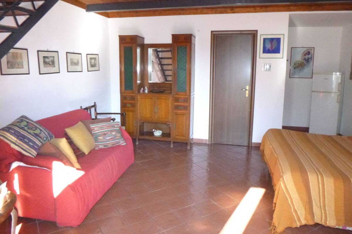 A bedroom with a red sofa, a bed with a striped blanket, a wooden cabinet, and a staircase.