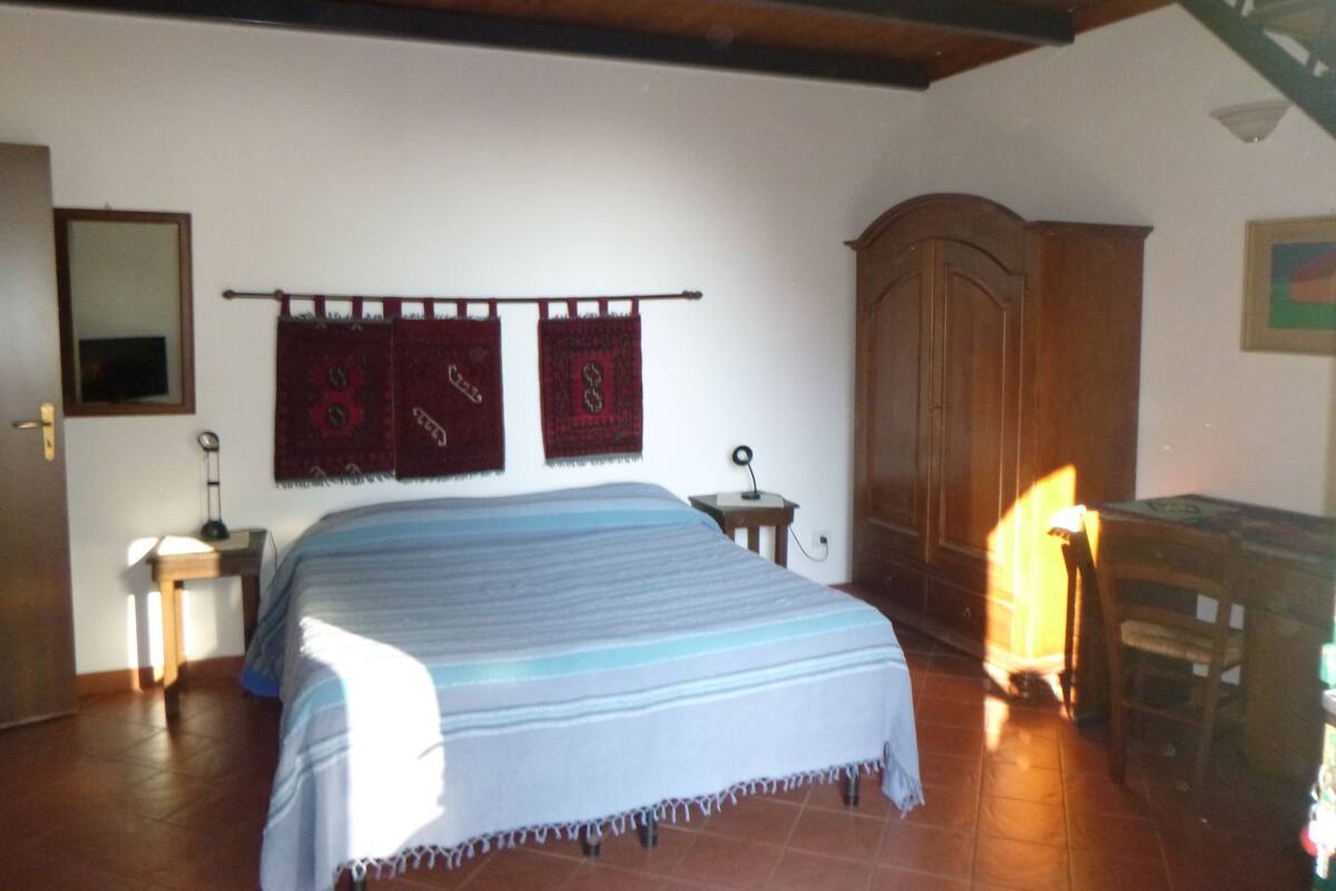 A bedroom with a bed, wooden wardrobe, and a desk with a lamp.