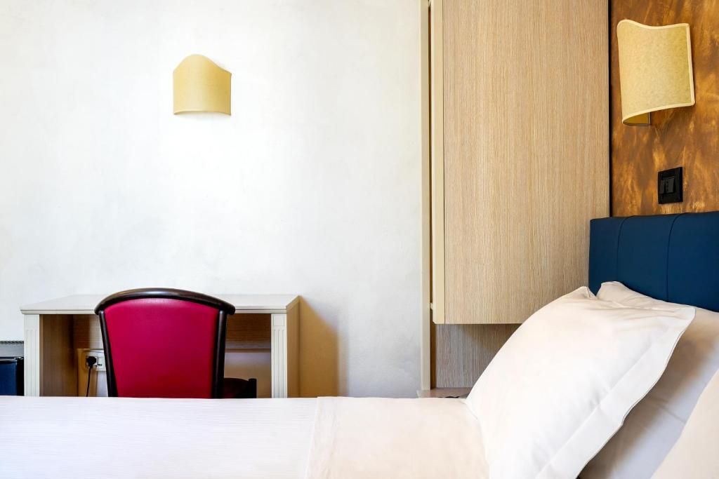 A hotel room with a bed, a desk, a red chair, and a wardrobe.