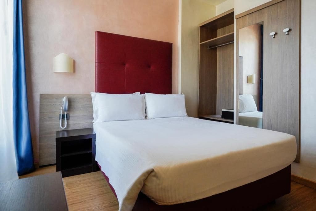 Una habitación de hotel con una cama grande, un teléfono en la mesita de noche, un armario y un espejo.