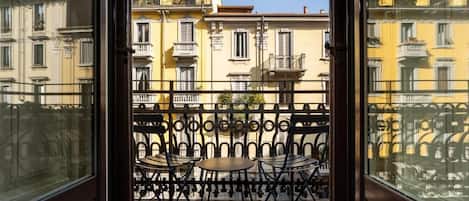 A balcony with a view of yellow buildings, a metal railing, and two tables with chairs.