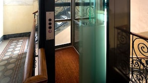 An elevator with a glass door, a wooden handrail, and a metal railing with decorative patterns. - Panizza (Milan)