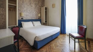 A hotel room with a bed, a desk, a chair, a wardrobe, and a window with curtains. - Panizza (Milan)
