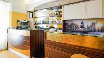 A bar area with a counter, shelves of bottles, and a painting of a historical building.