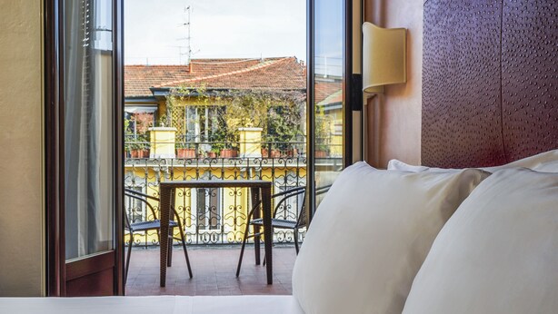 A hotel room with a large window, a balcony with a table and chairs, and a bed with white bedding. - Panizza (Milan)