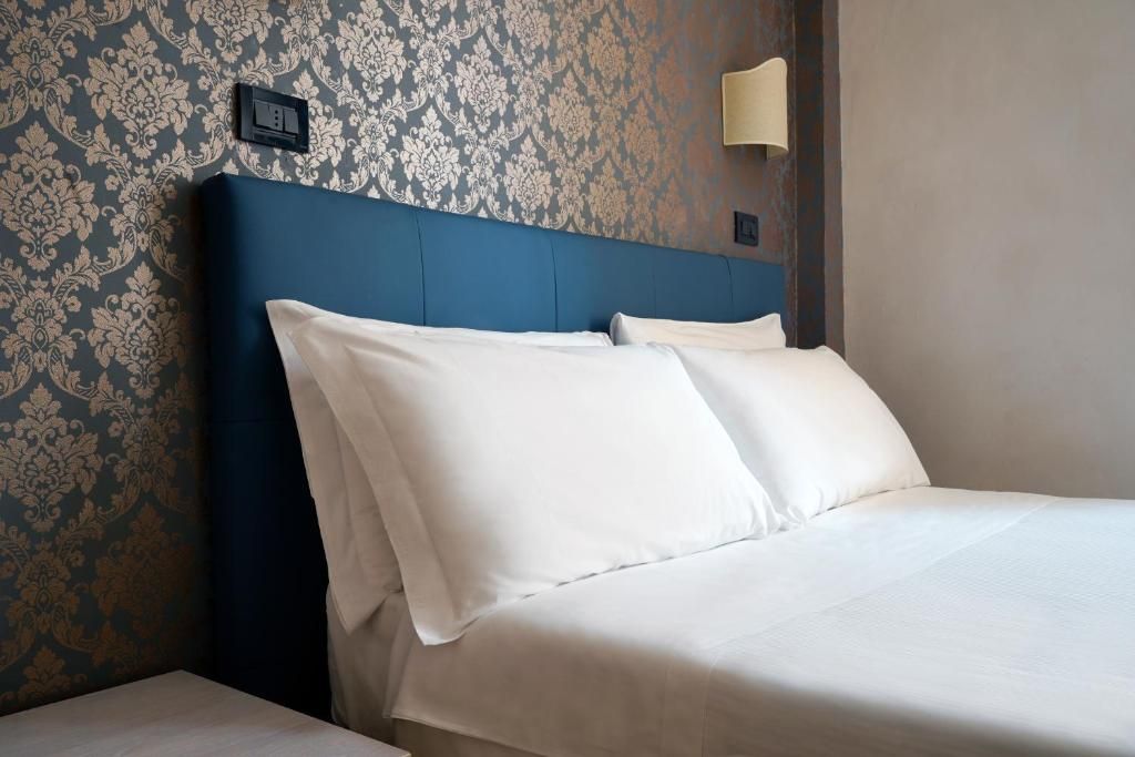 A hotel room with a bed, a nightstand, a wall-mounted light, and a power outlet.