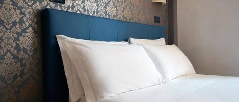A hotel room with a bed, a nightstand, a wall-mounted light, and a power outlet.