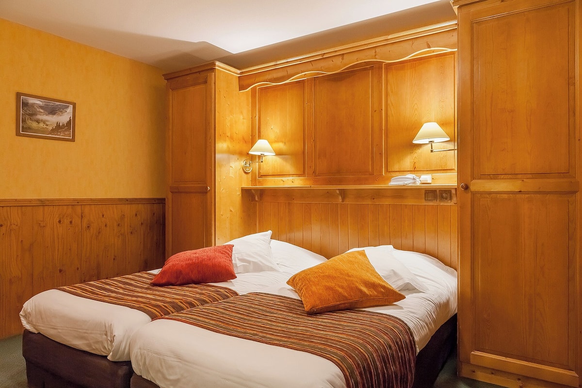 A wooden-paneled room with a bed, two wall-mounted lamps, and a framed picture on the wall.