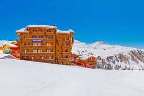 A multi-story wooden building with balconies, a restaurant sign, and a ski slope in the background. - Hotel Les Balcons Village & Spa Belle Plagne (La Plagne-Tarentaise)