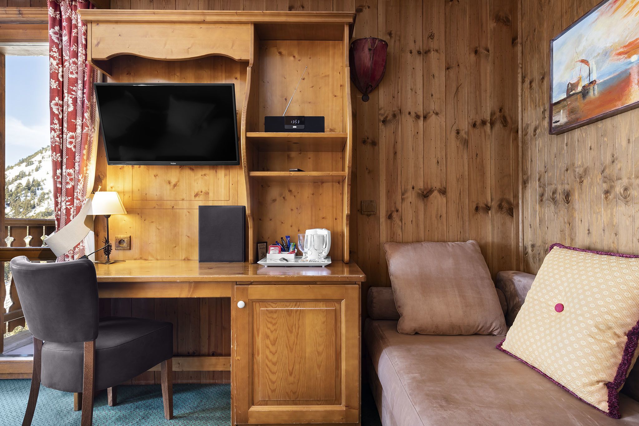 A wooden cabin interior with a TV, a desk with a lamp, a coffee maker, and a couch.