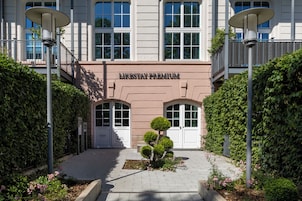 Um edifício com uma placa indicando 'LIKESTAY PREMIUM', uma pequena árvore e um caminho pavimentado.