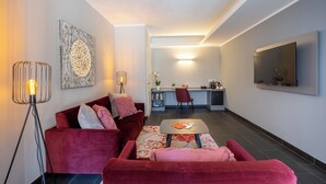Una sala de estar moderna con un sofá rojo, una mesa de centro y una lámpara de pie. Se observa un área de cocina al fondo con una mesa de comedor y sillas.