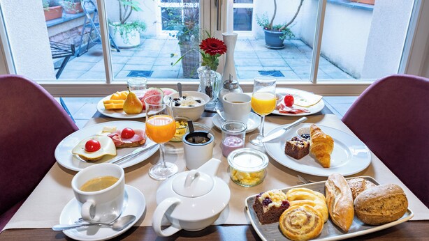 Una mesa de desayuno con diferentes alimentos, una tetera y vistas al exterior.