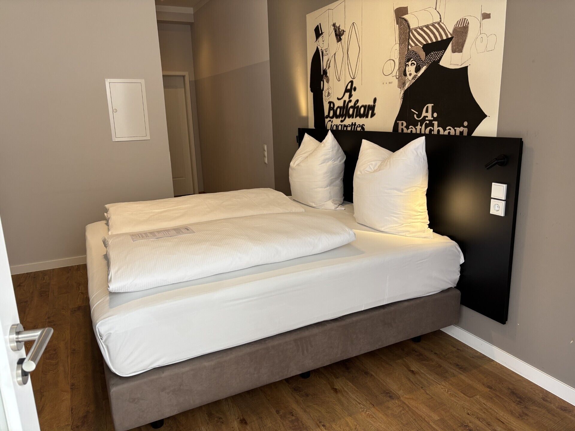 A modern hotel room with a large bed, a headboard, a door, and a wall with a poster.