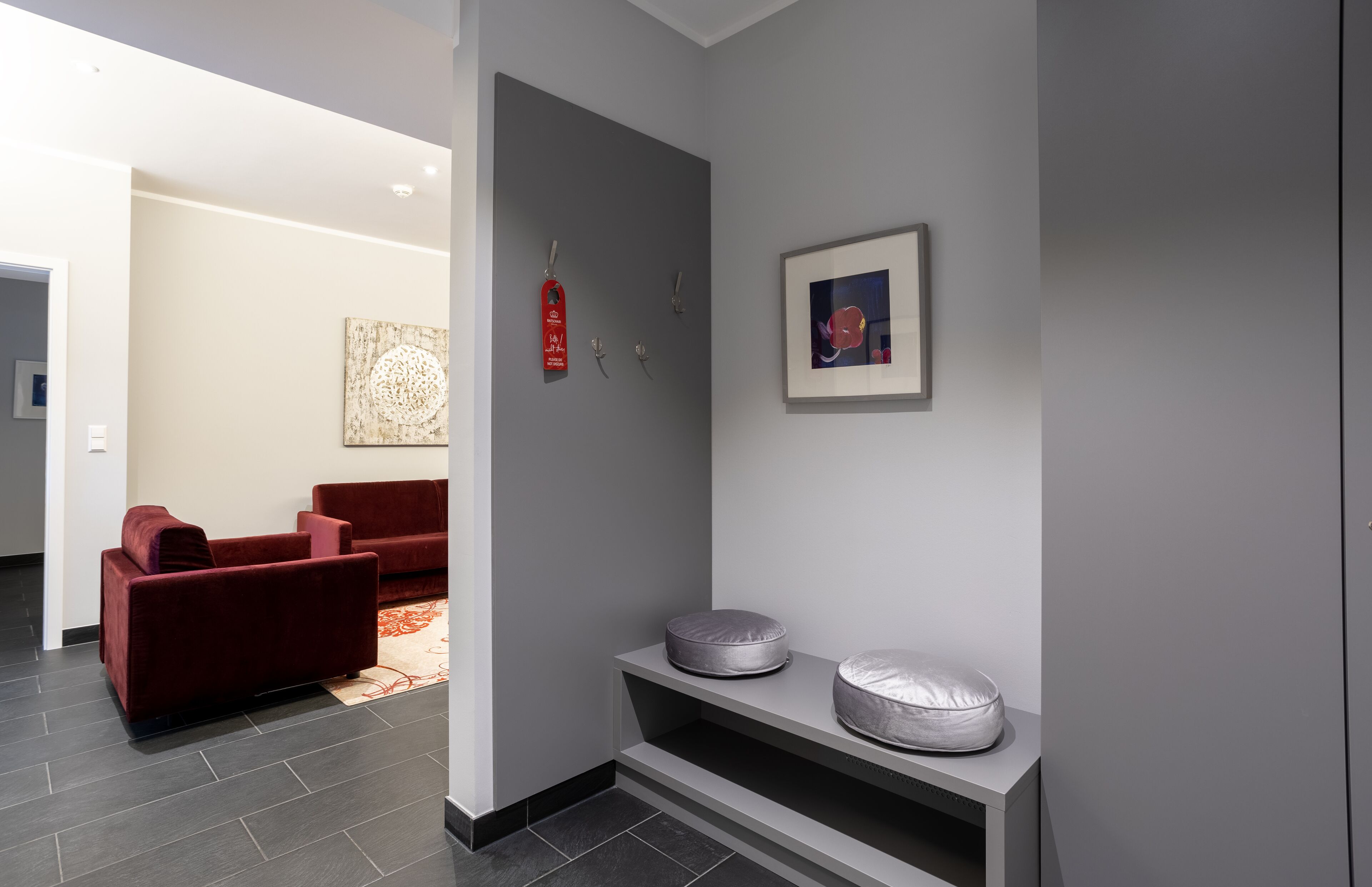 A modern living room with a red sofa, a grey wall with a framed picture, and a shelf with two cushions.