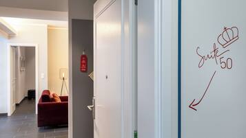 A hallway with a red sofa, a floor lamp, and a door with a fire alarm.