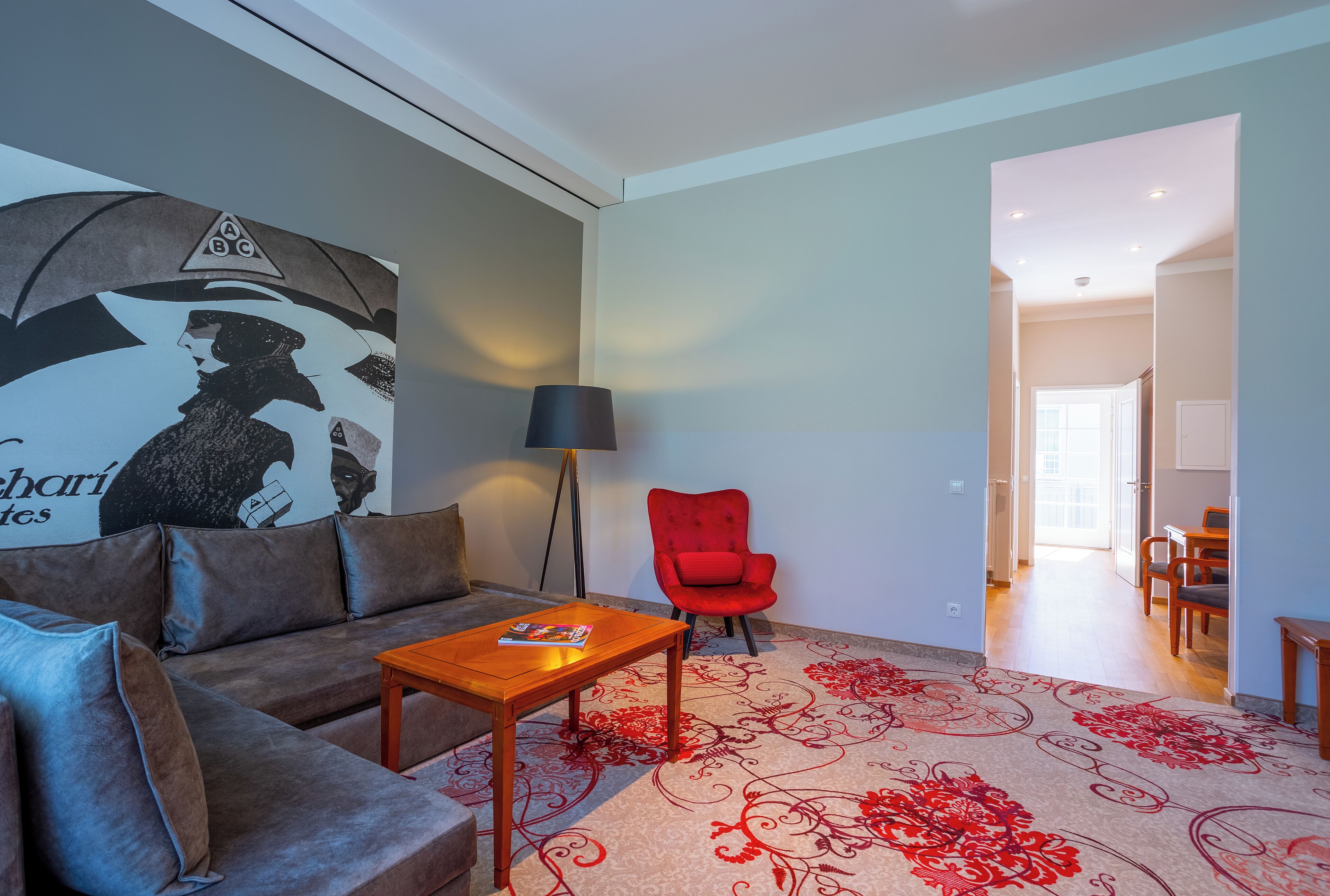 Een woonkamer met een bank, een rode fauteuil, een salontafel en een vloerlamp.