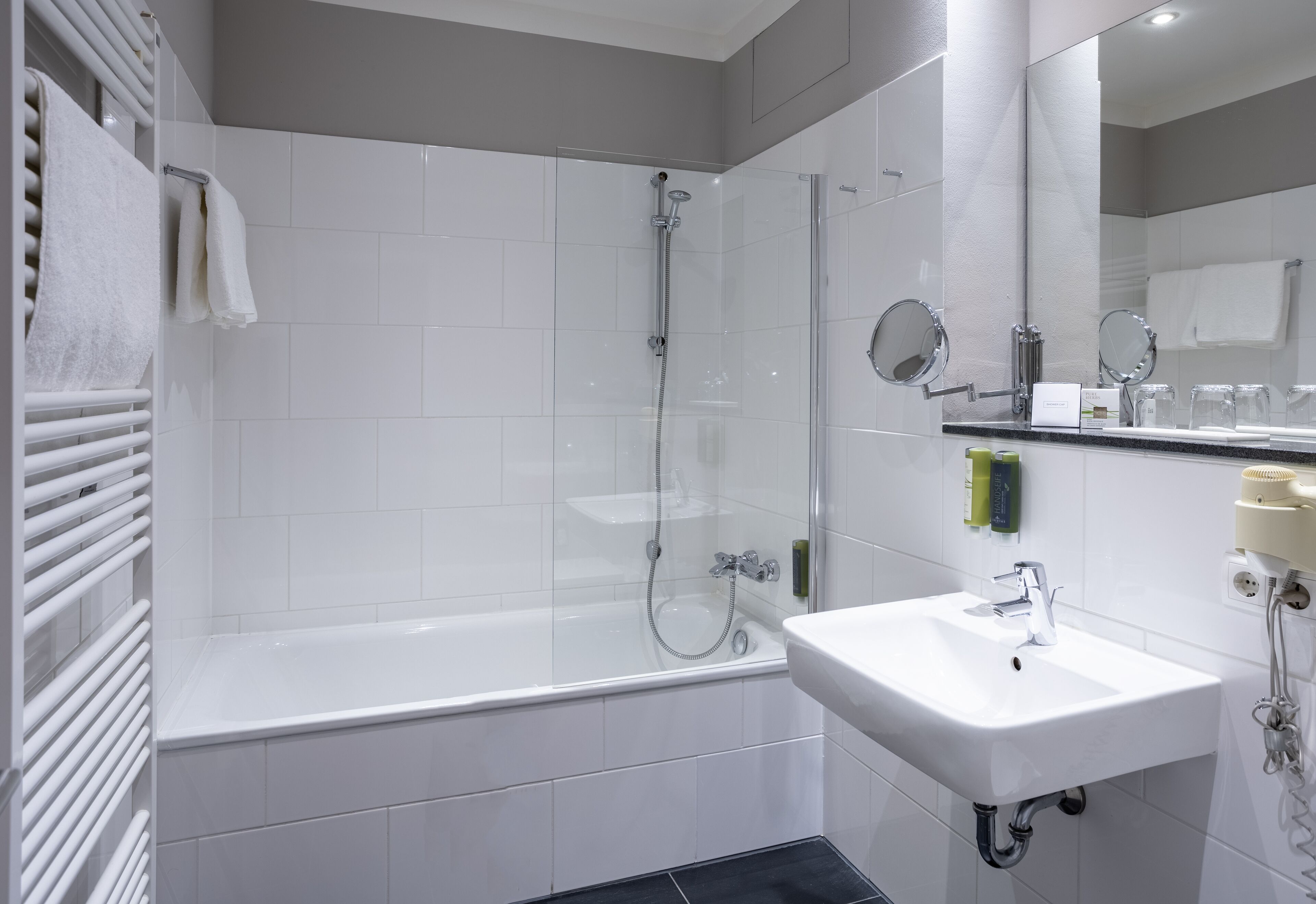 A modern bathroom with a glass-enclosed shower, a white sink, and a mirror with a round frame.