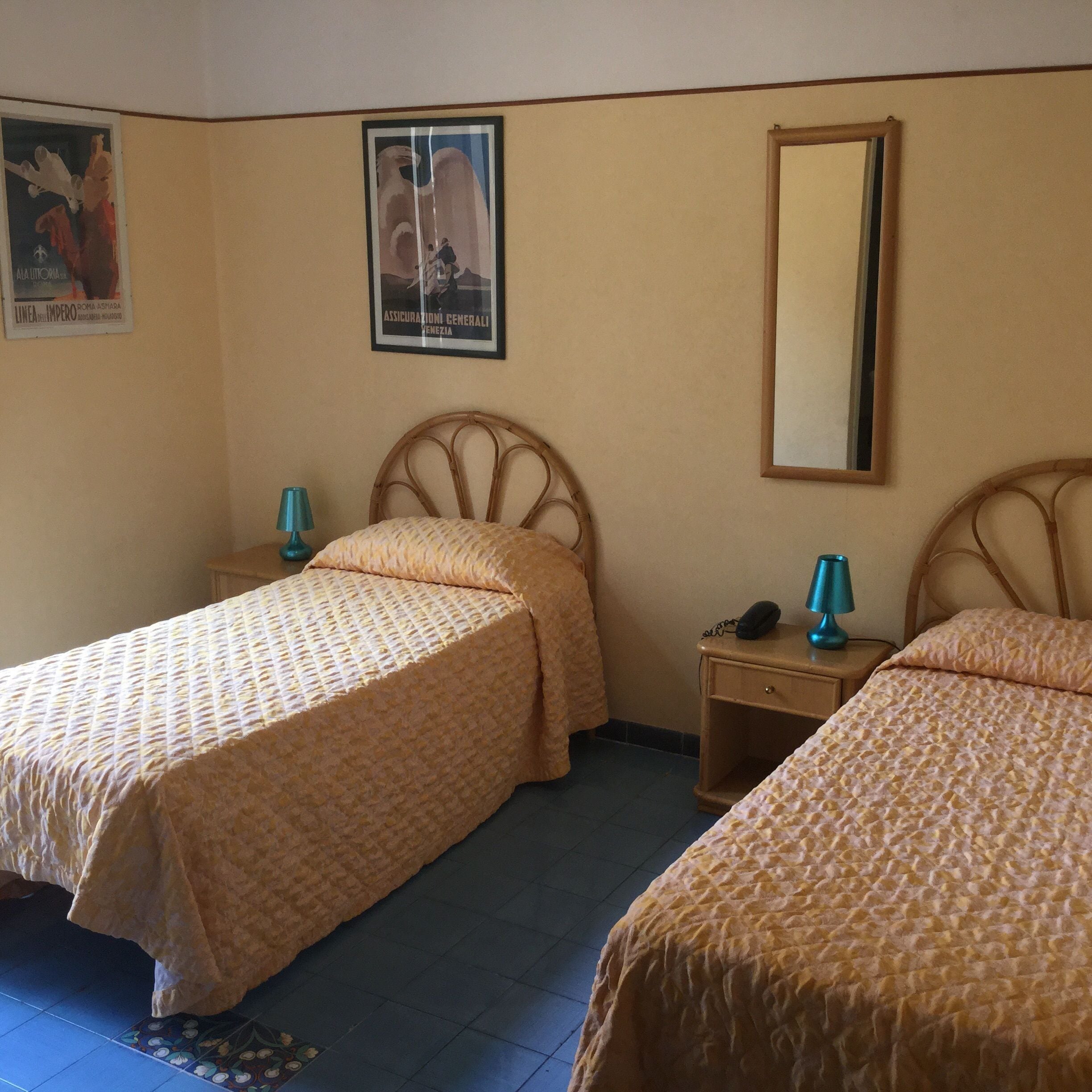 A room with two beds, a nightstand with a lamp, a mirror, and a poster on the wall.