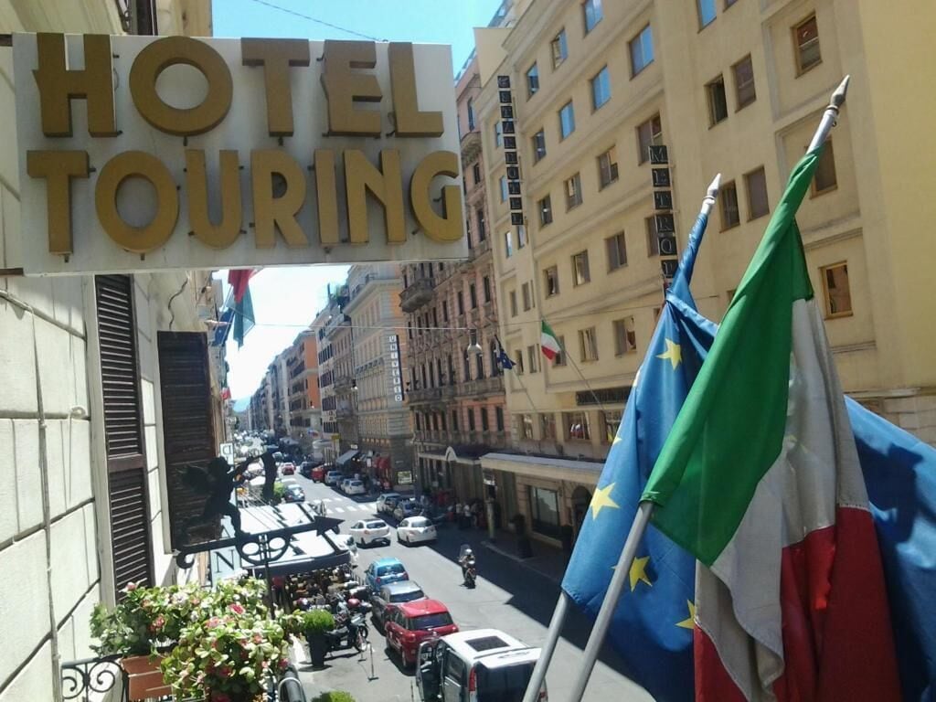 Une enseigne d’hôtel avec l’inscription « HÔTEL TOURING » et des drapeaux.