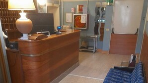 Un espacio habitable compacto con un mostrador de recepción de madera, un sofá azul, un tapete estampado y una pequeña kitchenette al fondo.