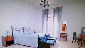 Un dormitorio con cama, mesita de noche, lámpara, silla y televisor.