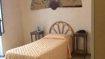 Une chambre à coucher comprenant un lit, une table de chevet et une commode, ainsi qu’un ventilateur fixé au mur.