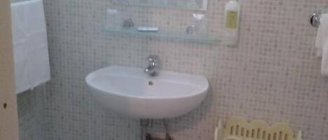 Un baño con lavamanos, espejo y dispensador de papel higiénico.