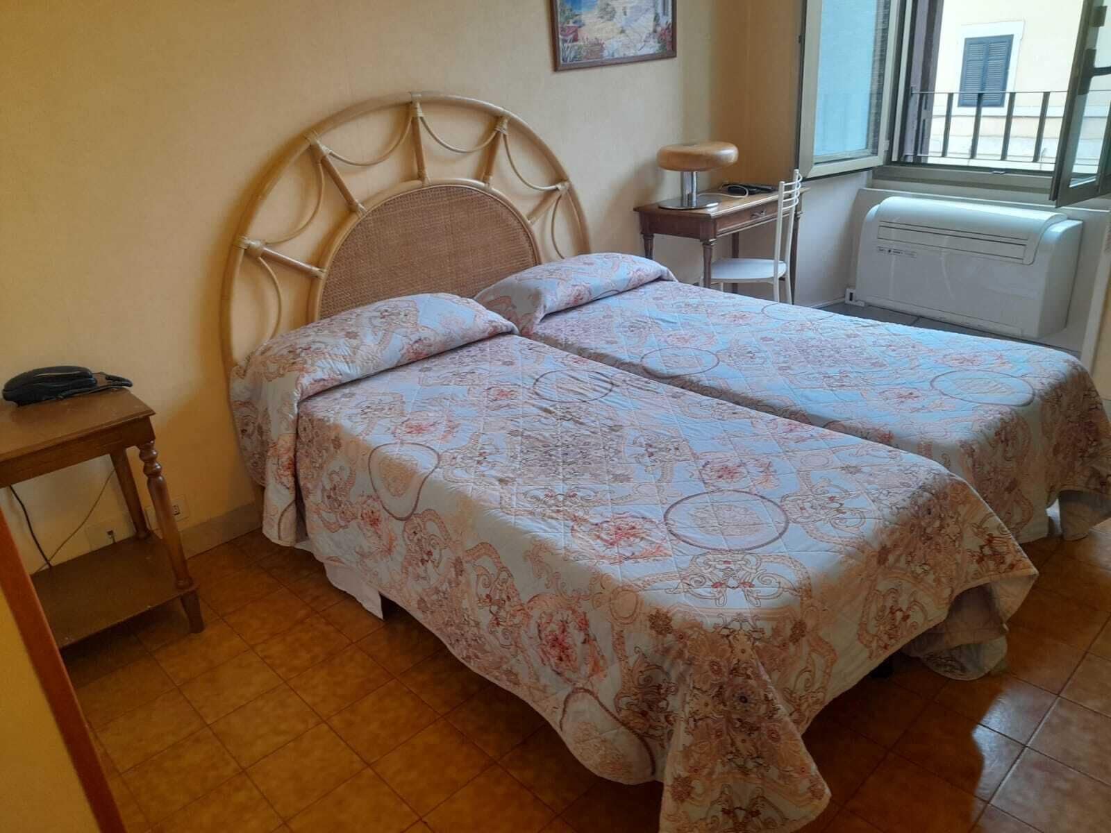 A room with two beds, a small table, a chair, and a radiator.