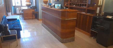 Un vestíbulo de hotel con un mostrador de recepción de madera, una zona de estar con sofás azules, una mesa de comedor y una cocina con estufa.