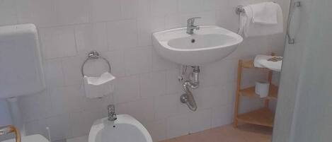 Un baño con inodoro, bidé, lavamanos y ducha.