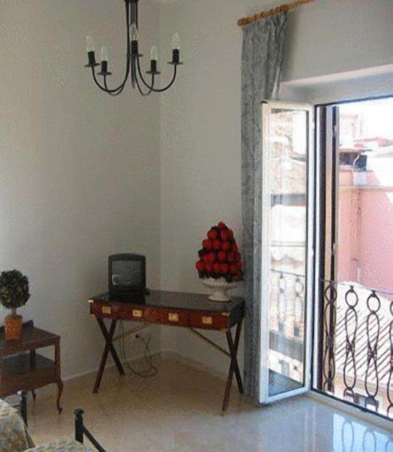 A room with a chandelier, a table with a decorative item, a small plant, and a view through a glass door.