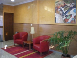 A lobby with two red armchairs, a small table, a floor lamp, and a potted plant. - La Noyesa (O Grove)