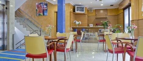 Un vestíbulo de hotel con una recepción, una escalera y varias mesas de comedor con sillas.