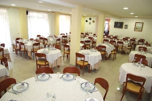 A dining area with round tables set for multiple people, chairs, and tables covered with white tablecloths. - La Noyesa (O Grove)