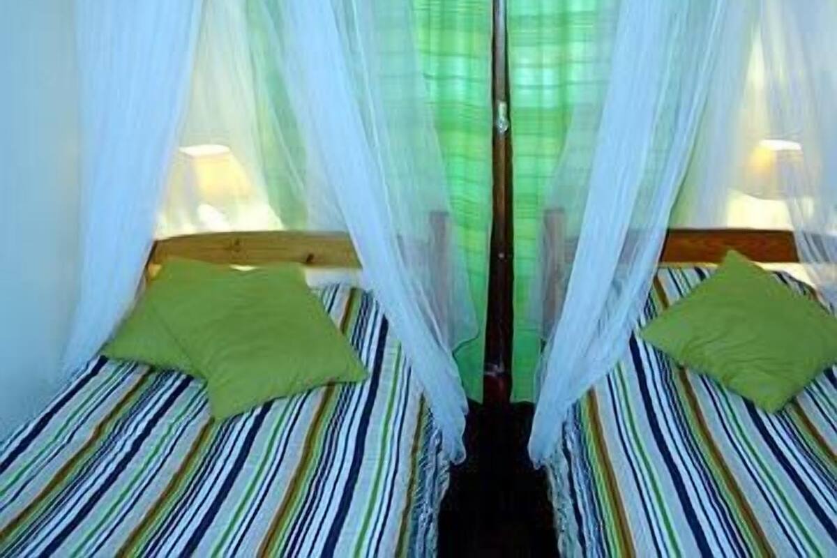 A room with two beds, each with a green pillow and striped bedding.