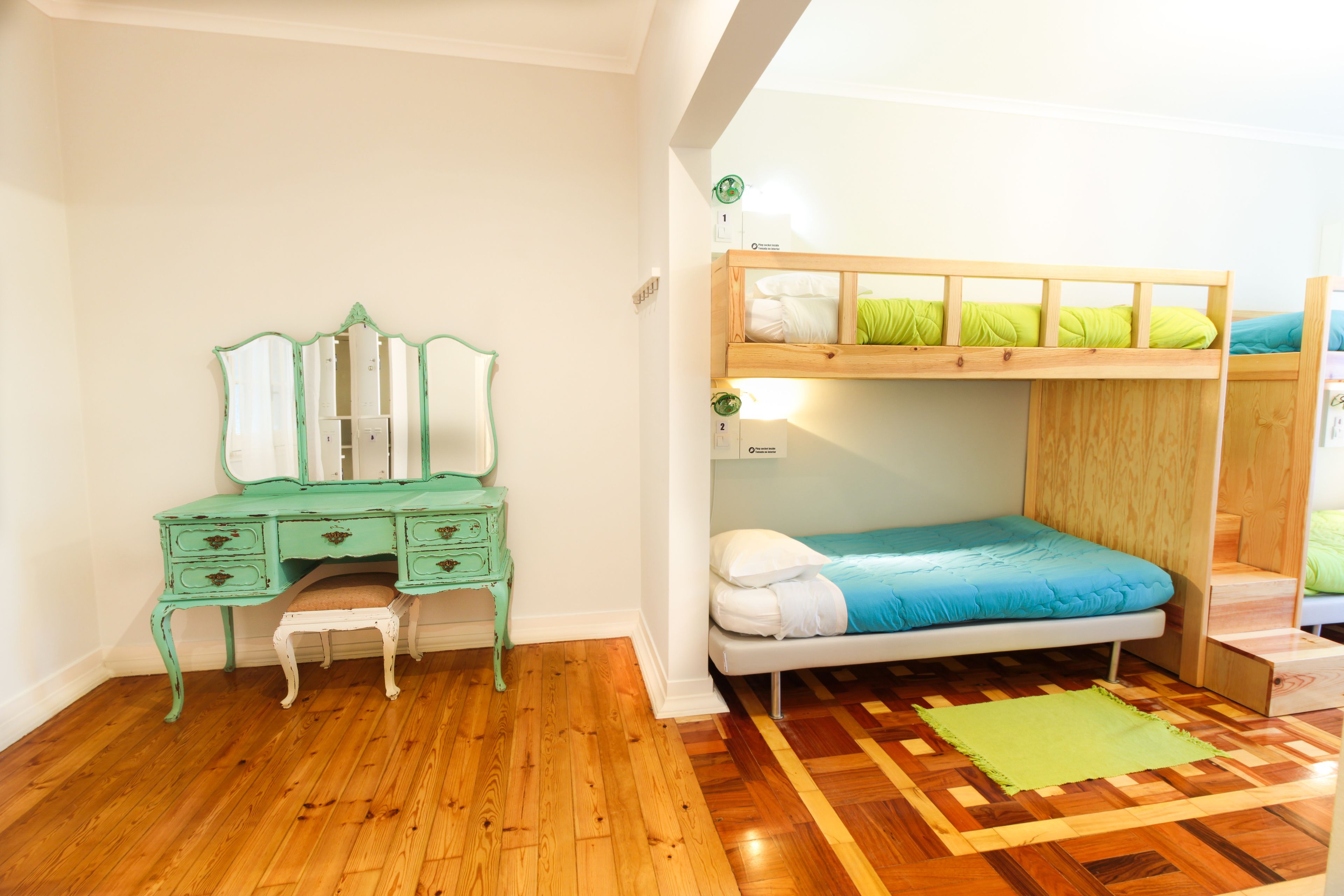 Um quarto com uma cama beliche, um aparador verde com espelho e um tapete estampado.