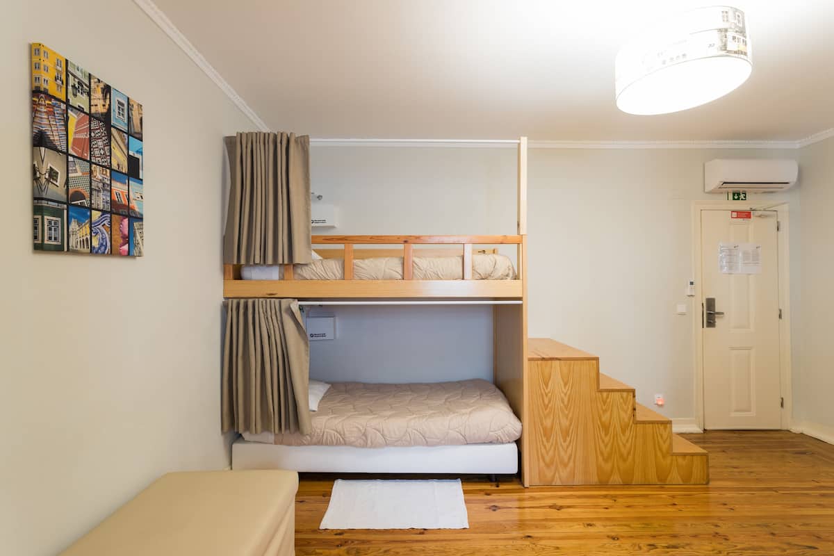 Een slaapkamer met stapelbedden, een houten trap, een witte deur met een nooduitgangsbordje en een wandairconditioner.