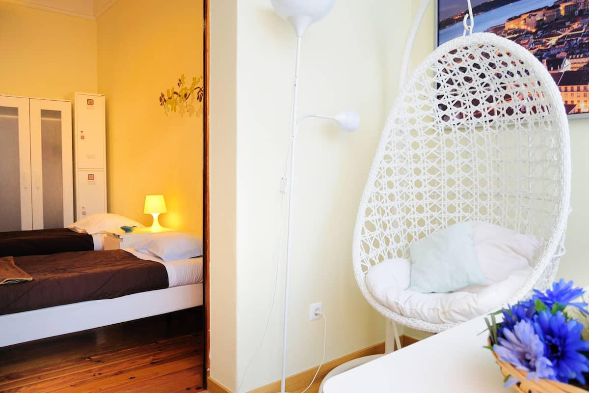 Een kamer met twee bedden, een hangstoel, een lamp en een wandlamp.