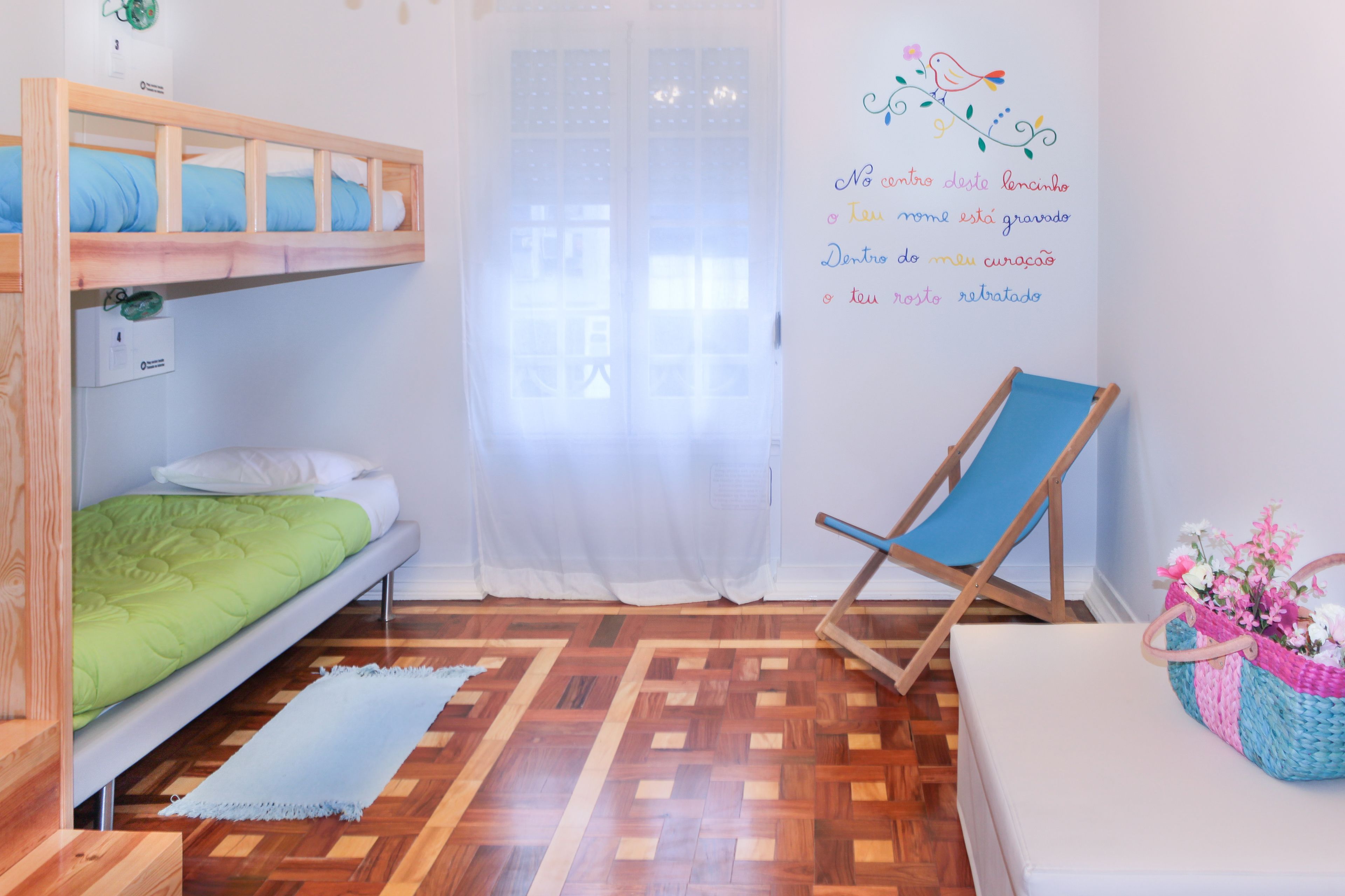 A room with a bunk bed, a single bed, a blue chair, a white sofa, a wooden floor, and a wall with a decorative sticker.