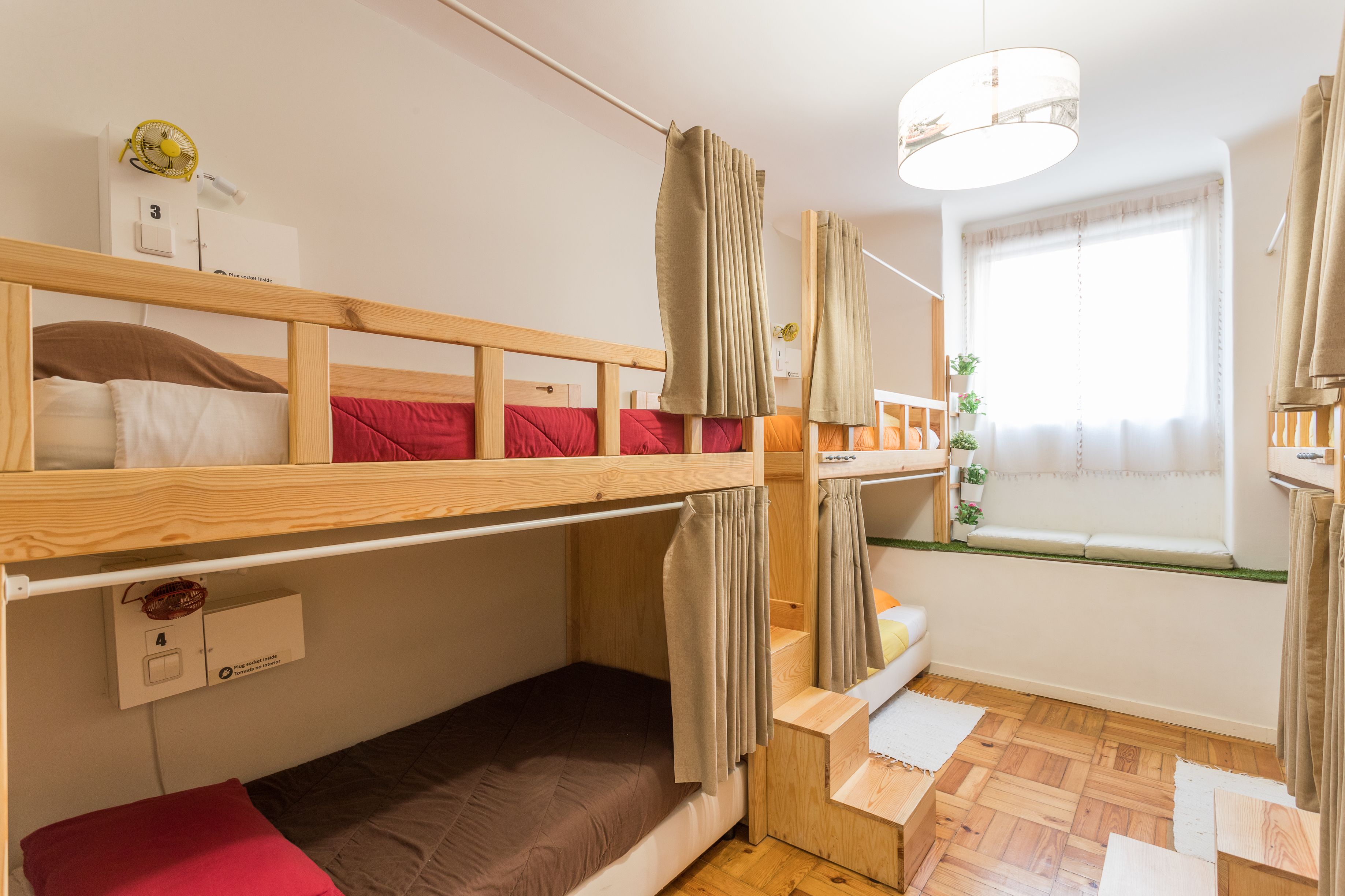 Une chambre avec un lit superposé, une fenêtre, un ventilateur et un petit bureau.