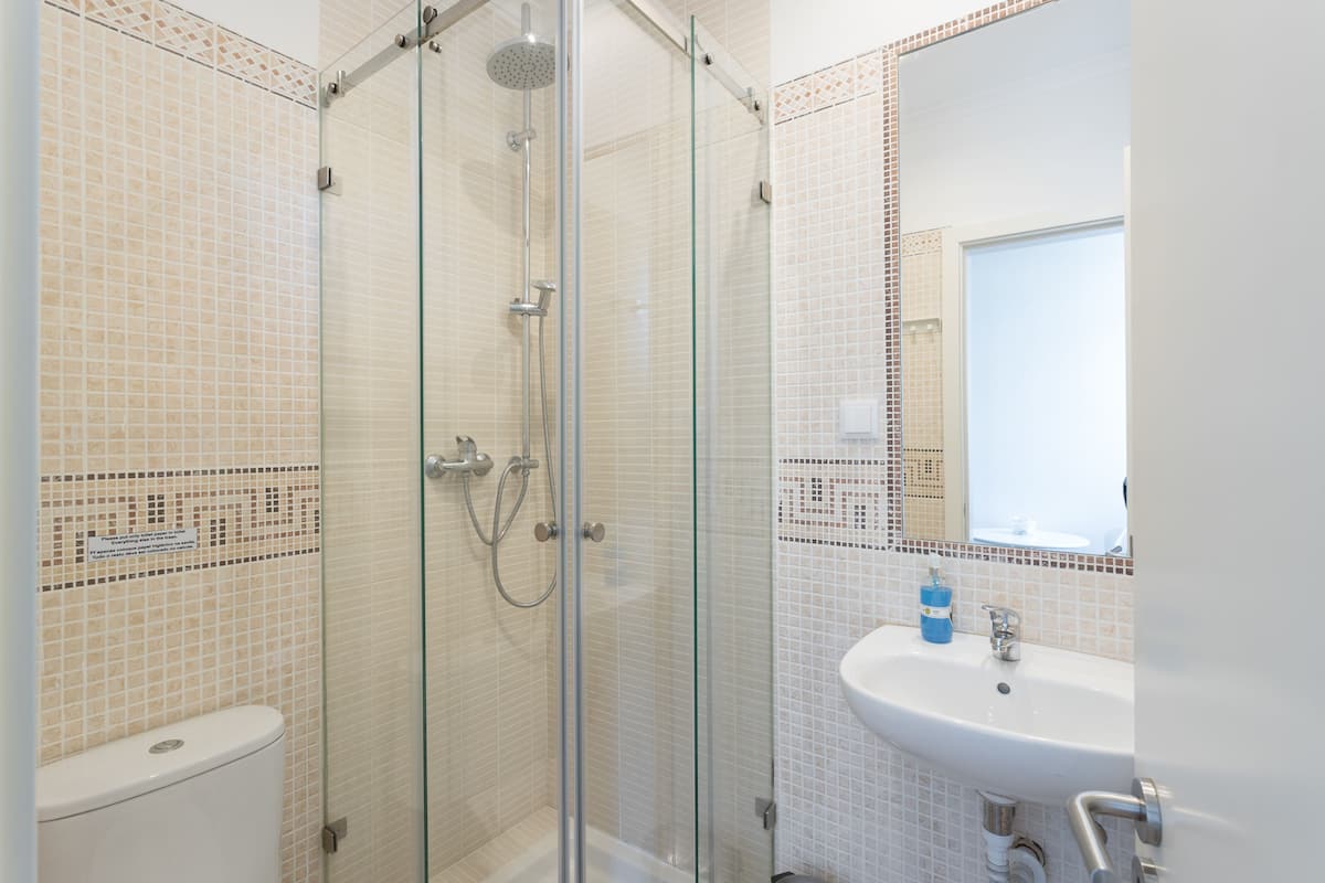 Een badkamer met een glazen douchecabine, een wit wastafelmeubel en een betegelde muur.