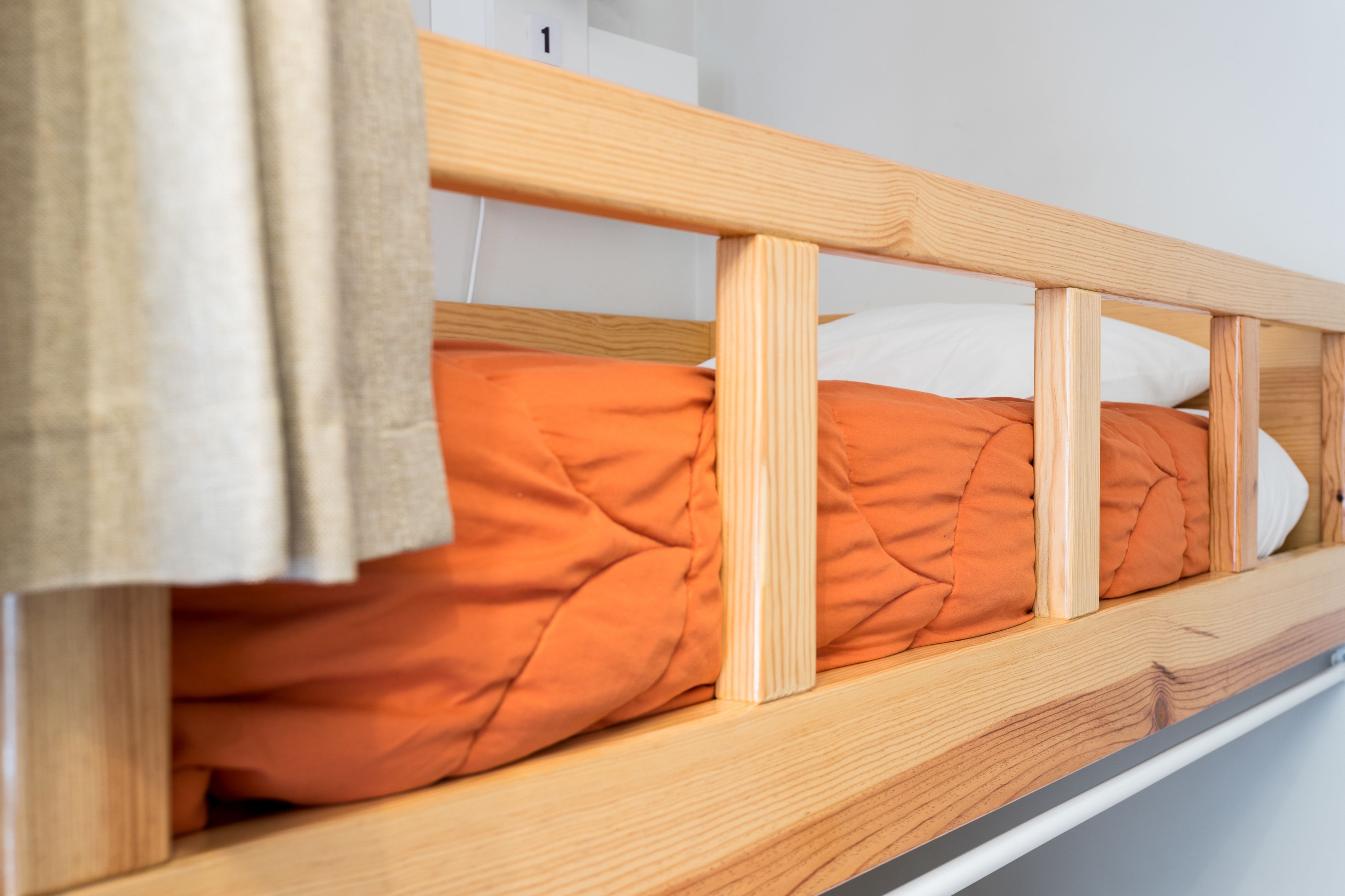 A wooden bunk bed with orange bedding and a white pillow.