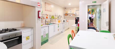 A modern kitchen with white cabinets, a gas stove, and a microwave. There is a dining area with a white table and green chairs.