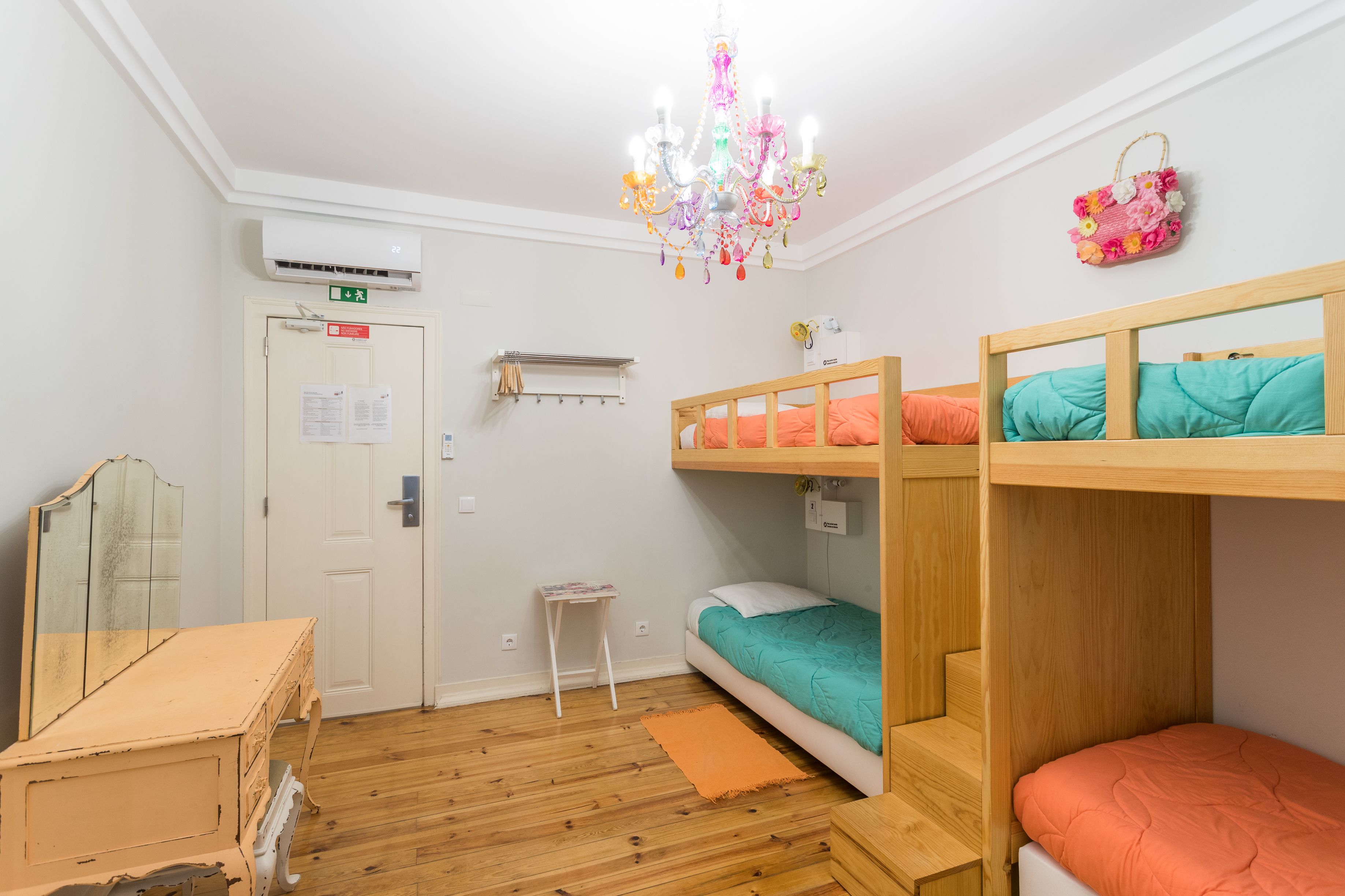 A room with bunk beds, a small table, a mirror, a chandelier, and a door with an emergency exit sign.